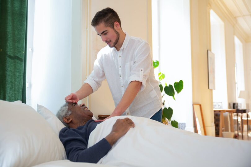 a man in white shirt standing beside an elderly lying on the bed