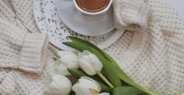 flowers and cup of cacao placed on knitted cardigan on bed